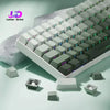 Vista cercana de un teclado mecánico blanco con teclas cian degradadas e iluminación RGB sobre una superficie verde claro.
