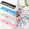 A hand is using a portable manual paper cutter with various colored blades to trim paper for crafting and scrapbooking.