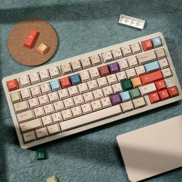 A close-up view of a white mechanical keyboard with retro PBT keycaps in various colors resting on a teal surface.