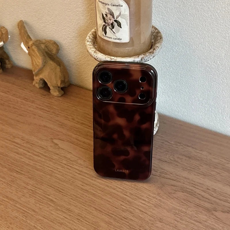 A brown leopard print phone case is displayed next to a candle in a rustic setting.