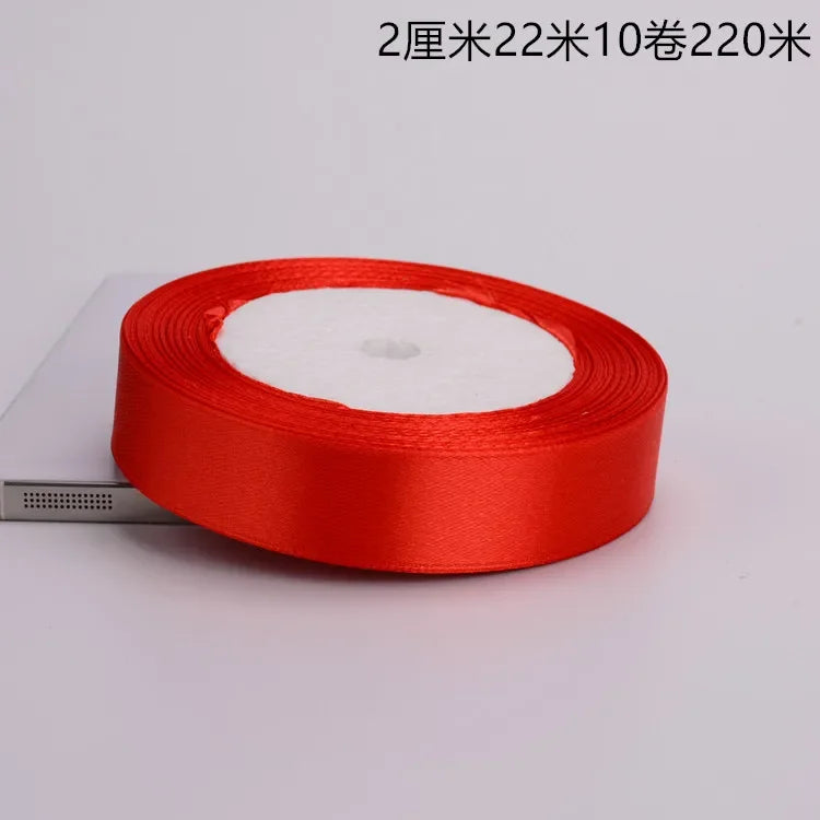 A roll of red satin ribbon with a white center core is shown on a white background.