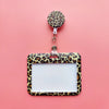 A leopard print ID holder with a clear plastic frame and a matching lanyard keychain on a pink background.