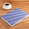 A purple notebook lying on a wooden surface next to a white cup and saucer.
