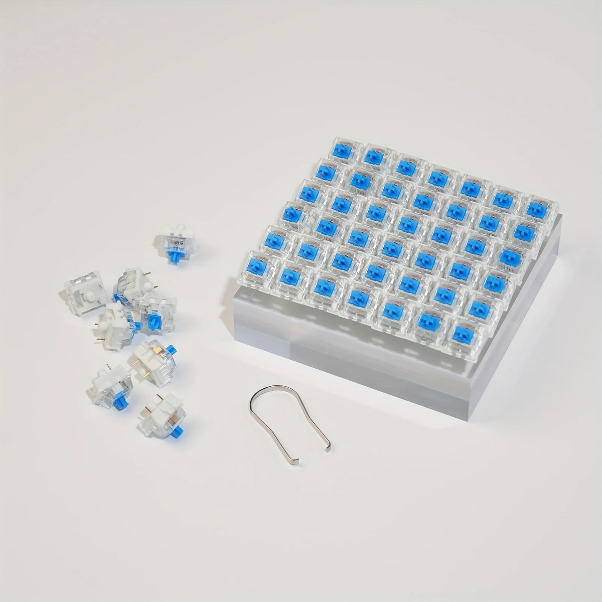 A tray of blue mechanical keyboard switches and a keycap puller set are displayed on a white surface.
