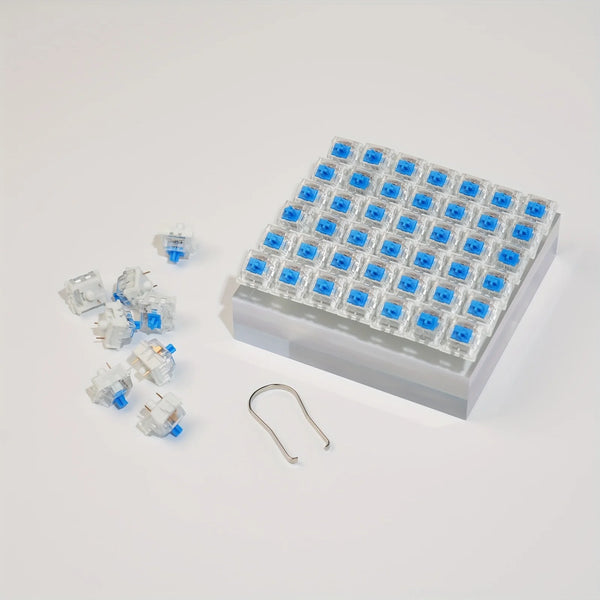 A tray of blue mechanical keyboard switches and a keycap puller set are displayed on a white surface.
