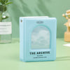 A light blue hollow photo card binder titled The Archive with a translucent cover resting on a green surface.
