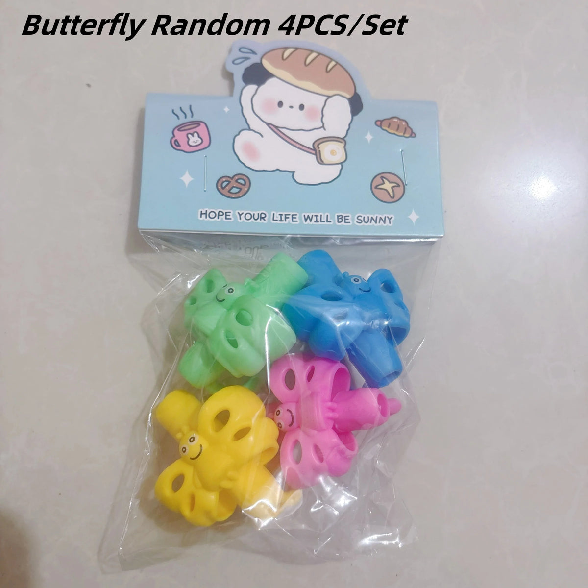 A set of four colorful silicone butterfly pencil grips for kids packaged in a clear plastic bag.
