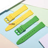 Three silicone watch straps in yellow and green colors are displayed on a light blue background.