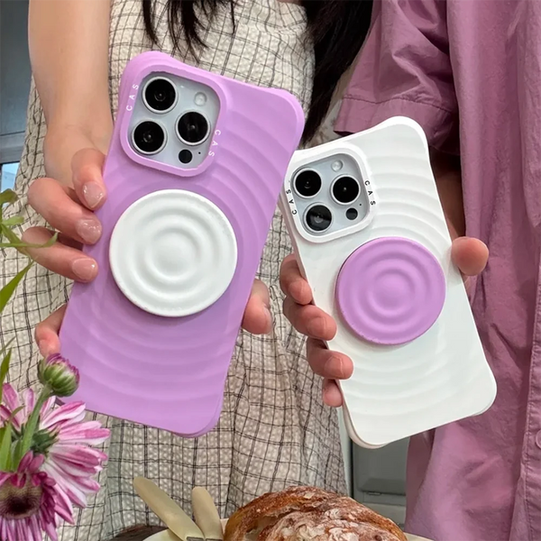 A hand holds a purple ripple grip magnetic phone stand with a silicone finish next to a white one.