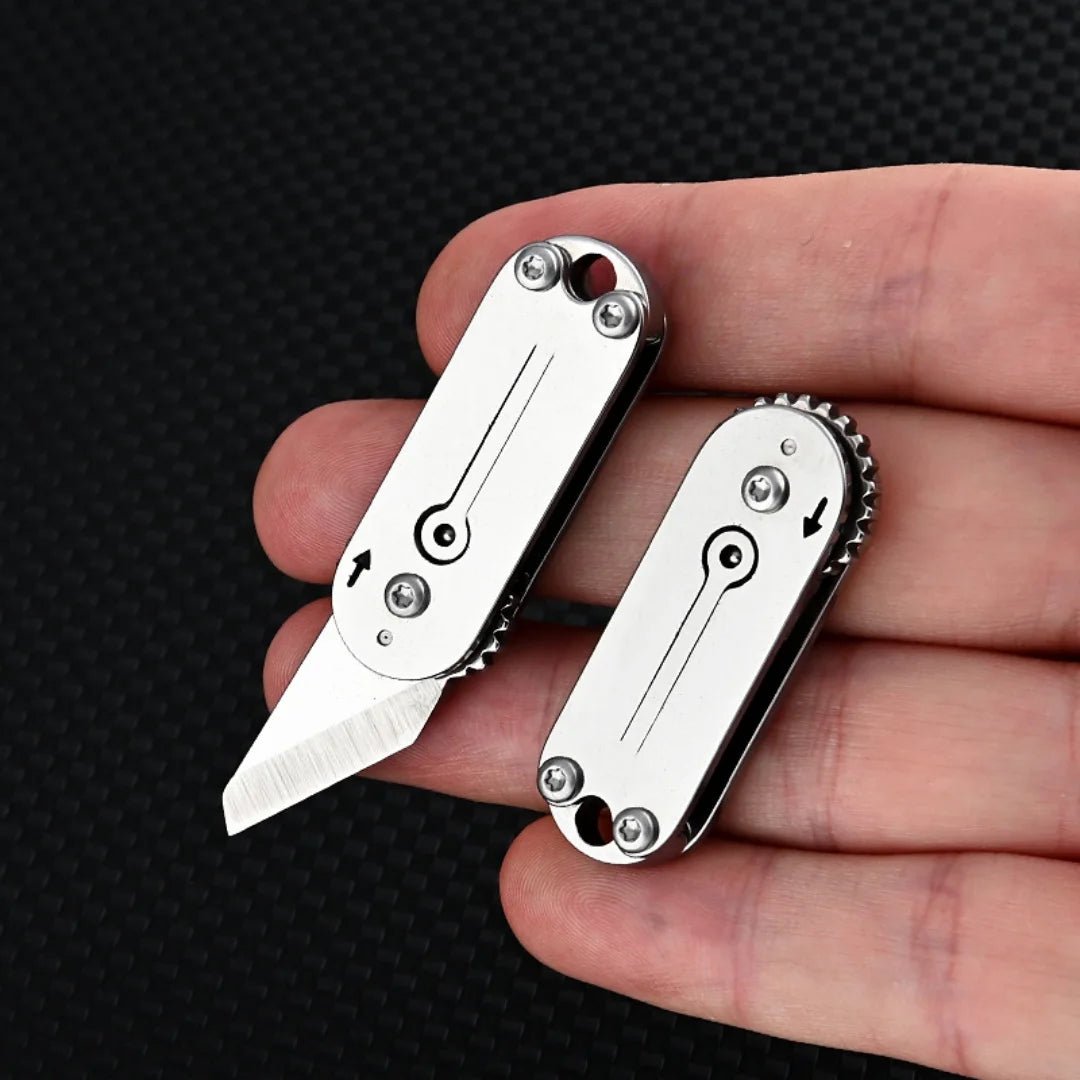 A hand holds a compact stainless steel pocket knife with a serrated blade and keychain attachment.