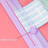 A close-up of a portable manual paper cutter trimmer showing a reference line on the plastic tool against a pink background.