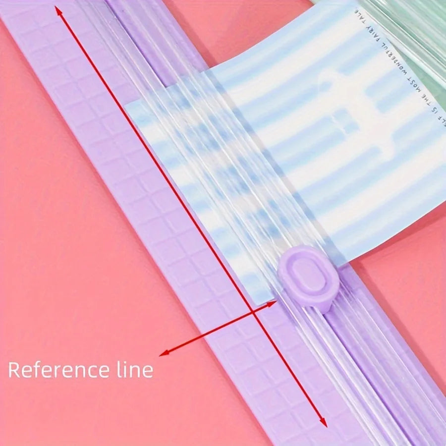 A close-up of a portable manual paper cutter trimmer showing a reference line on the plastic tool against a pink background.