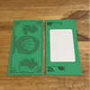 A green 3D printed shell card holder with an NFC tap-to-pay feature lying on a wooden surface.