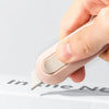 A hand is operating a pink portable mini paper cutter on a white surface.