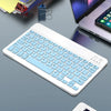Weiße Mini-Bluetooth-Tastatur und Maus-Kombination auf einem grauen Schreibtisch neben einem Laptop.