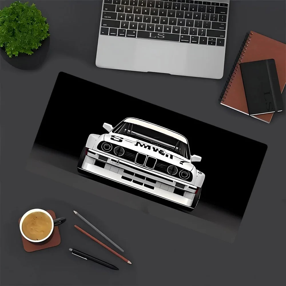 A white JDM car model is placed on a dark mouse pad next to a laptop and some stationery items.