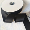 A roll of matte black satin ribbon for crafts, wrapping, and decor, lying on a white surface.