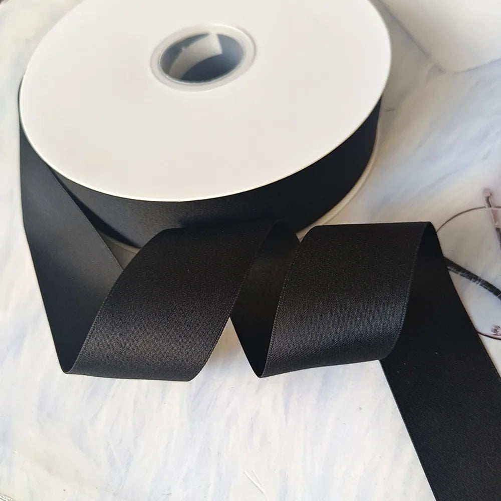 A roll of matte black satin ribbon for crafts, wrapping, and decor, lying on a white surface.