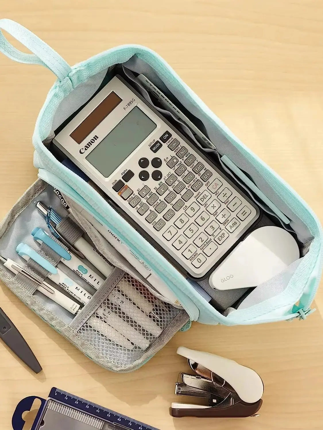 A light blue canvas pencil case is open, showing a Canon calculator and various pens and pencils inside.
