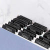 A collection of black laminated Bible tabs with biblical names and chapters laid out on a white marble surface.