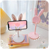 A pink rabbit mobile phone stand with a smartphone mounted on it, placed next to some books.