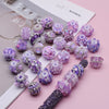 A collection of purple and lilac handmade acrylic flower beads for jewelry making displayed on a white card.