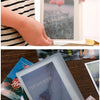 A hand holds an A6 photo storage booklet with a dark cover featuring delicate floral imagery.