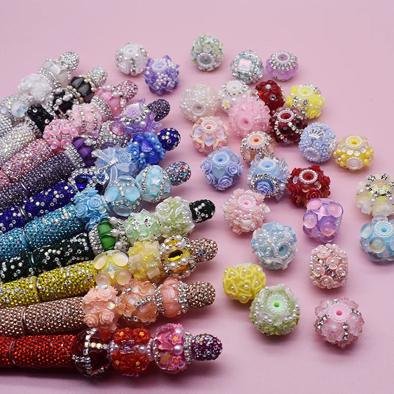 A collection of handmade acrylic flower beads in various shades of pink, purple, and yellow arranged on a light pink backgrou