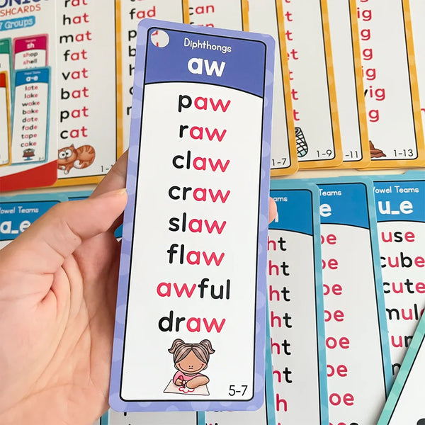 A hand holds up a purple phonics flashcard showing the diphthong aw with words like paw, raw, claw, and awful.