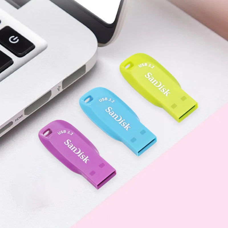 Three SanDisk Ultra Shift USB 3.2 flash drives in yellow, blue, and purple lying on a white surface.