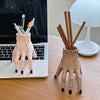A hand-shaped decoration made of pink resin palm with wooden pencils inside, displayed on a desk.
