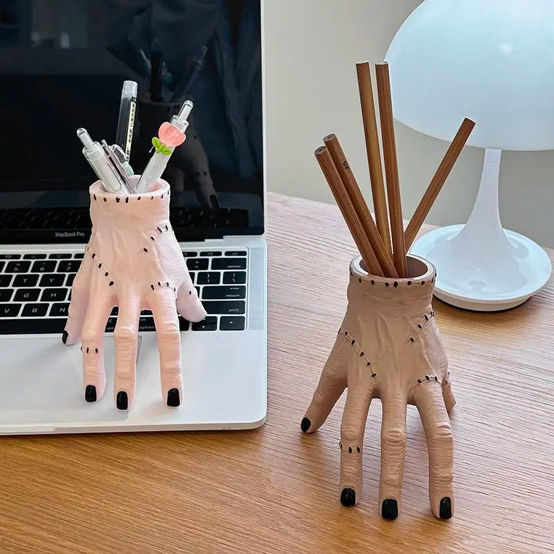 A hand-shaped decoration made of pink resin palm with wooden pencils inside, displayed on a desk.