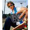 A young man holds a black magnetic wireless charging lens protector case for an iPhone outdoors.