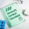 A green marble budget binder with a gold clasp and cash envelopes is shown on a white surface.
