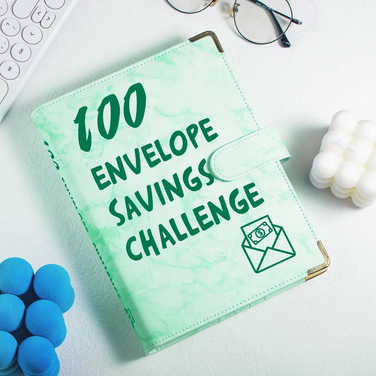 A green marble budget binder with a gold clasp and cash envelopes is shown on a white surface.