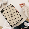 A black polka dot protective case for an iPad is being held by a hand on a white table.