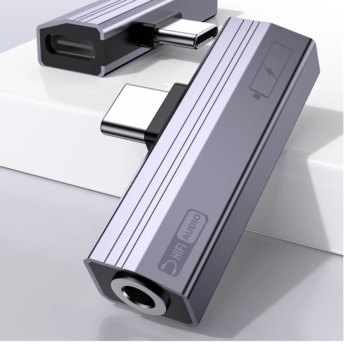 A silver audio adapter with a USB-C connector is shown resting on a white surface.