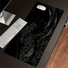 A black desk mouse pad featuring a white line drawing of a crashing wave and sea foam, with a white computer mouse resting on