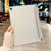 A clear protective case for an iPad is held by a hand in a dimly lit indoor setting.