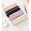 A collection of stacked pencil cases in pink, black, purple, and beige, with a gold-tipped pencil brush nearby.