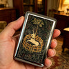 A hand holds a vintage stainless steel card and cash case featuring an ornate gold silhouette of a deer within a woven circle