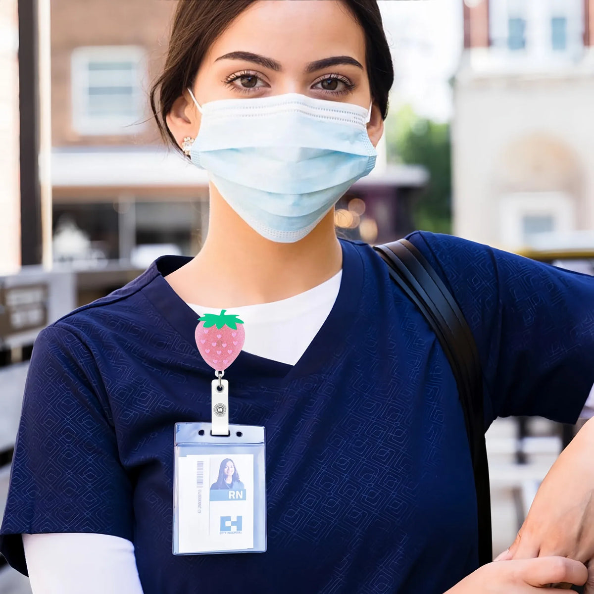 A woman in blue scrubs wearing a badge reel with a strawberry design.