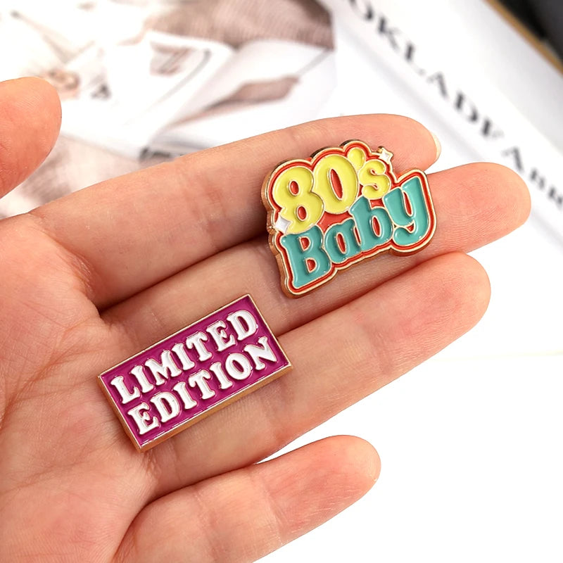 A set of colorful enamel pins featuring an 80s baby design and a limited edition badge, held in a hand.