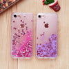 A pair of clear phone cases featuring pink and purple glitter with heart and star designs resting on a wooden surface.