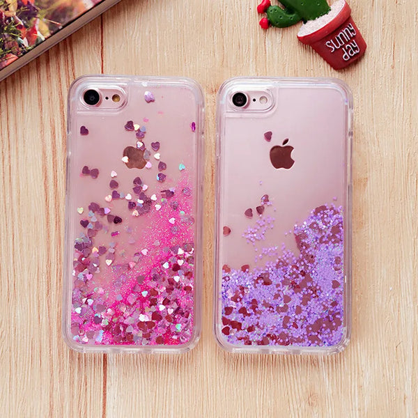 A pair of clear phone cases featuring pink and purple glitter with heart and star designs resting on a wooden surface.