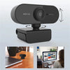 A black HD webcam device is shown with a camera module, positioned above a laptop and on a wooden desk.