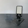 A black desktop stand for a phone or tablet with a rotating adjustable mount.