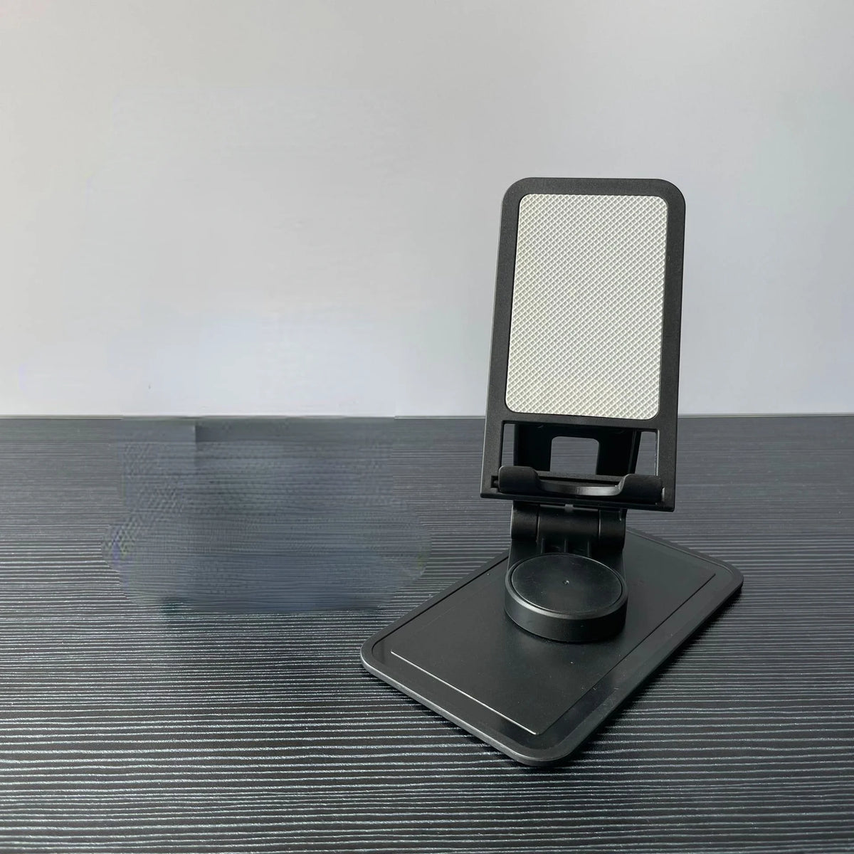 A black desktop stand for a phone or tablet with a rotating adjustable mount.