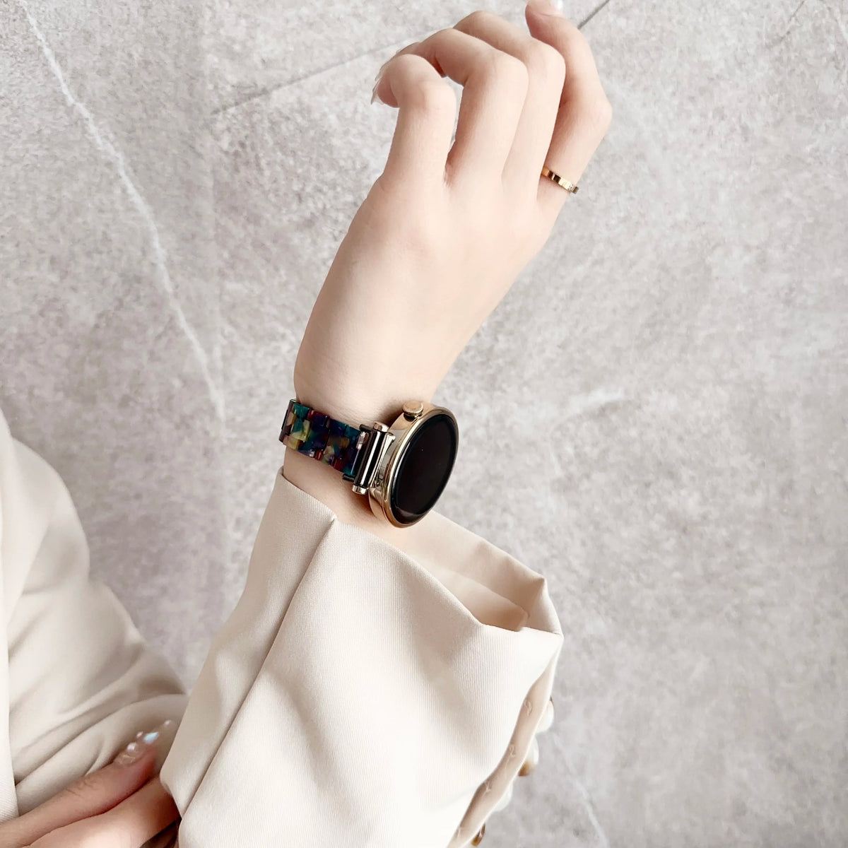 A hand wearing a resin beaded watch band with a three-bead design on a wrist, next to a light-colored blazer sleeve.