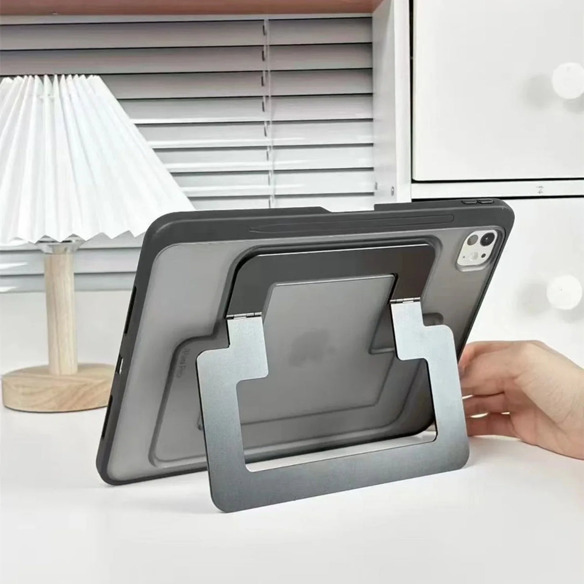 A gray protective case for a tablet or iPad is shown resting on a white surface next to a lamp and a kitchen cabinet.